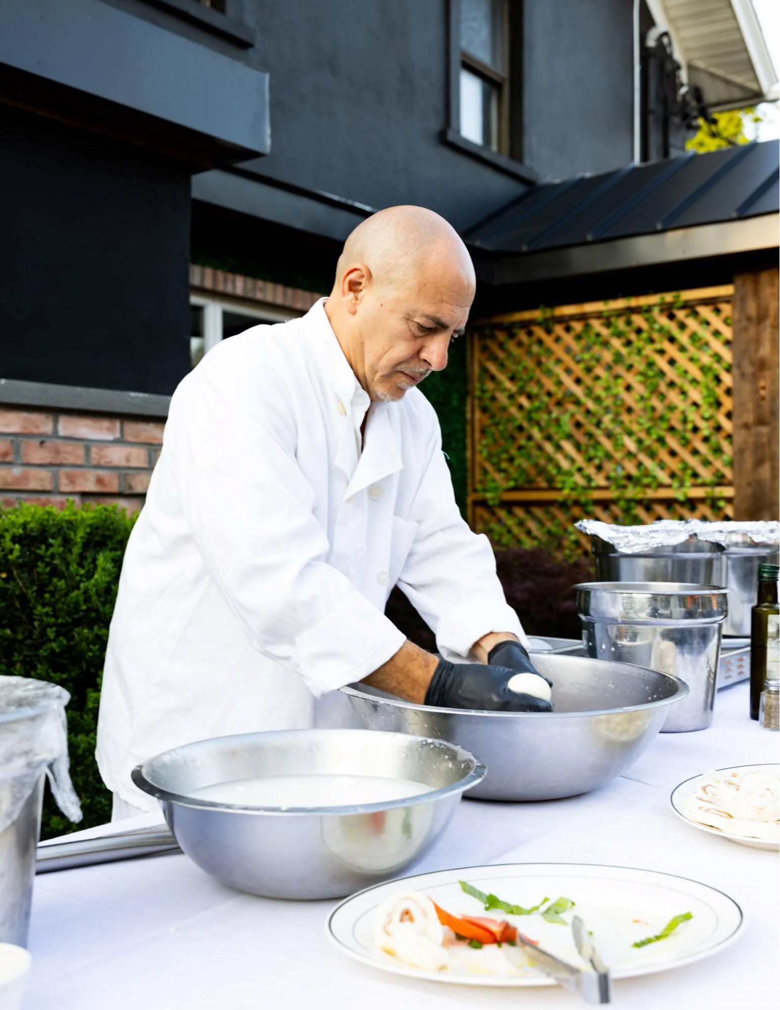 A chef in white hand-pulling fresh mozzarella at an outdoor prep table.