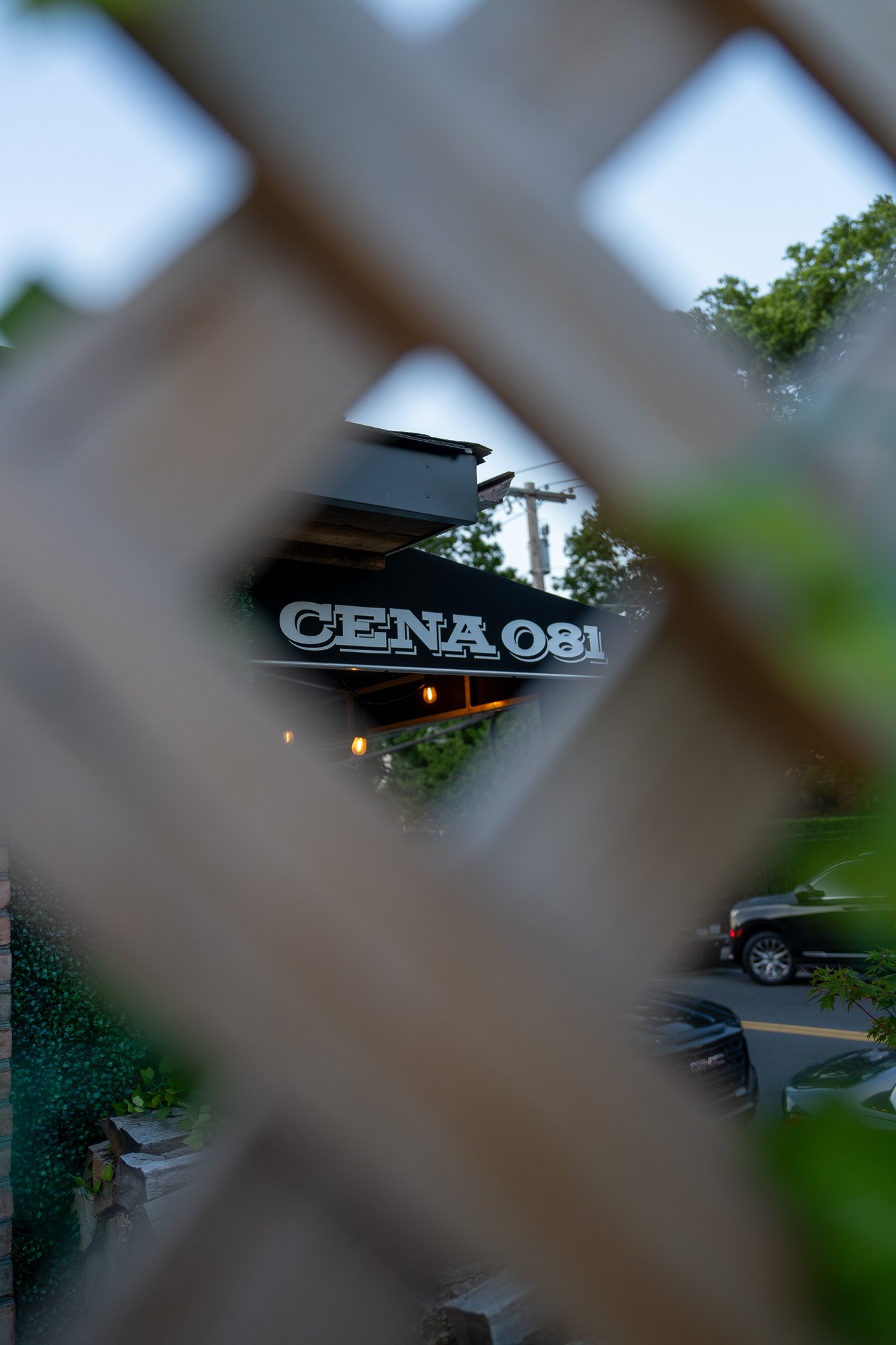 Exterior sign reading CENA 081, seen through a wooden lattice screen.