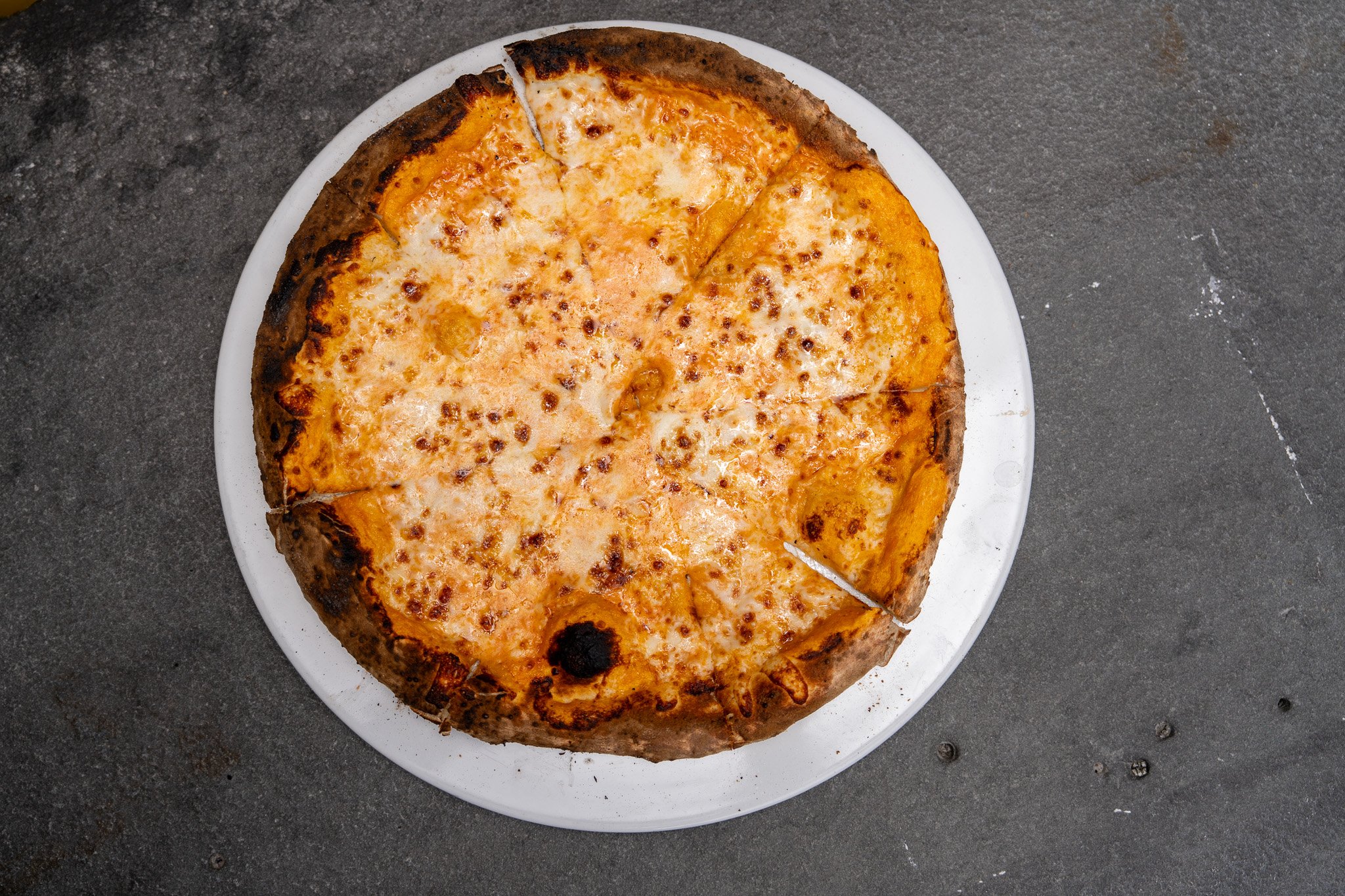 A cheese pizza with a golden-brown crust, served on a white plate on a dark surface.