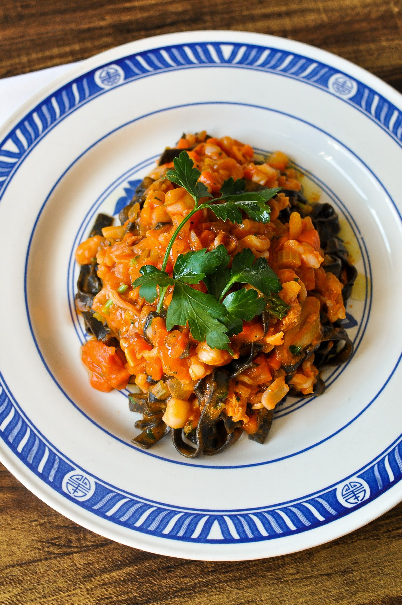 A white plate with blue decorative border containing a serving of vegetable stew topped with parsley, on a wooden table.